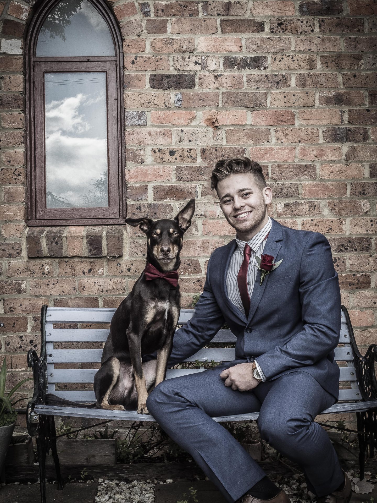 Man in suit sits next to a dog at a wedding. 